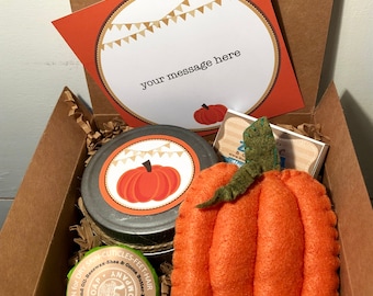 May include: A gift box filled with fall-themed items. Includes a felt pumpkin, a jar with a pumpkin label, a card with the text "your message here", and other products. The box is filled with brown paper.