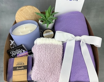 May include: A gift basket filled with lavender-scented items, including a candle, soap, and a throw blanket. The basket also includes a small potted succulent plant and a card that says "I love you Mom".