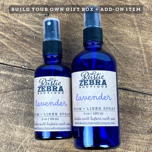 May include: Two blue glass spray bottles of lavender room and linen spray. The bottles have black spray nozzles and labels that read "Rustic Zebra Boutique" and "lavender". The larger bottle contains 4 oz (120 ml) and the smaller one contains 2 oz (59 ml).