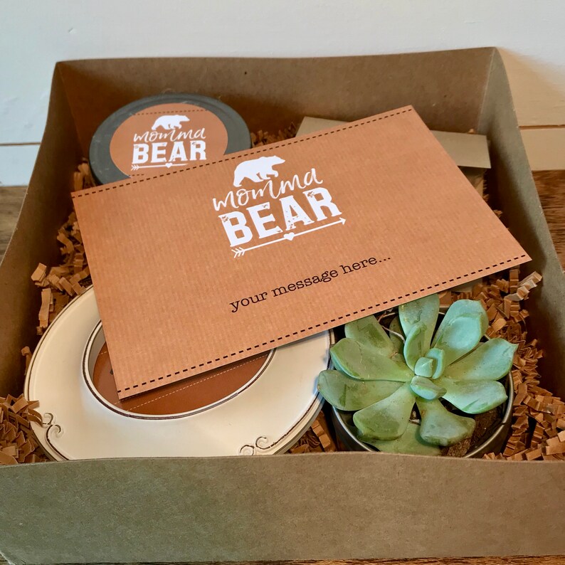 May include: A brown gift box filled with brown shredded paper, a white ceramic plate, a small potted succulent plant, and a card with the text "Momma Bear" and a space for a message.