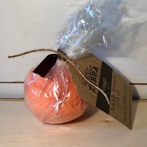 May include: An orange bath bomb, wrapped in clear cellophane and tied with twine and a brown ribbon. A brown tag with the text "Rustic Zebra Boutique" and "Orange bath bomb 5 oz" is attached.