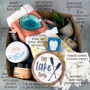 May include: A gift box filled with lake-themed items. Includes a small ceramic fish dish, a beach towel, a wooden lake sign, a candle, soap, and other self-care products. The box contains a variety of colors and textures, perfect for a relaxing day.