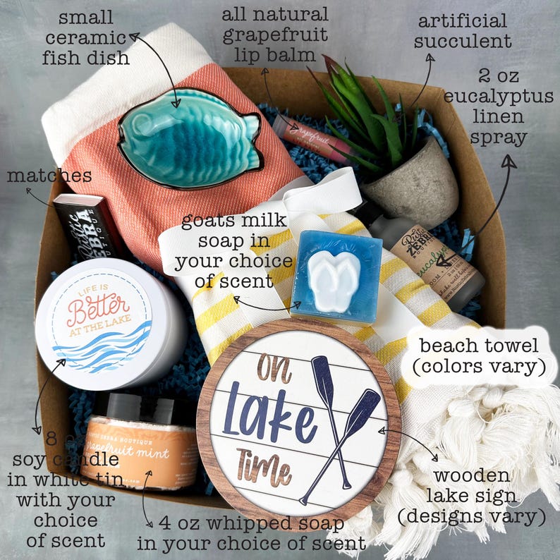 May include: A gift box filled with lake-themed items. Includes a small ceramic fish dish, a beach towel, a wooden lake sign, a candle, soap, and other self-care products. The box contains a variety of colors and textures, perfect for a relaxing day.