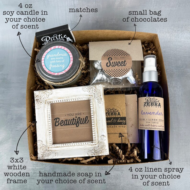 May include: A gift box filled with a 4 oz soy candle, a small bag of chocolates, a 3x3 white wooden frame, a bar of handmade soap, and a 4 oz linen spray. The box is filled with shredded paper and the items are arranged neatly. The candle is labeled "grandmas are moms with lots of frosting". The chocolates are labeled "You are Sweet". The frame is labeled "You are Beautiful". The soap is labeled "Rustic Zebra Boutique Real & Honey Handmade Soap". The linen spray is labeled "Rustic Zebra Boutique Lavender 100ml Linen Spray 4 oz | 120ml Shake well before each use".