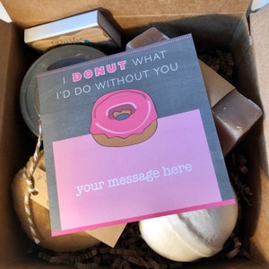 May include: A gift box filled with various items, including a bath bomb, soap, a jar of something, and a card that says "I donut what I'd do without you." The card has a pink and brown donut illustration and a space for a message.