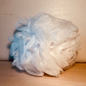Puede incluir: Un puff de ba&ntilde;o blanco hecho de un material suave de malla. El puff est&aacute; arrugado y parece nuevo.