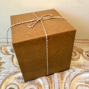 May include: A brown cardboard box with a white and brown twine bow. The box is tied with a single piece of twine.