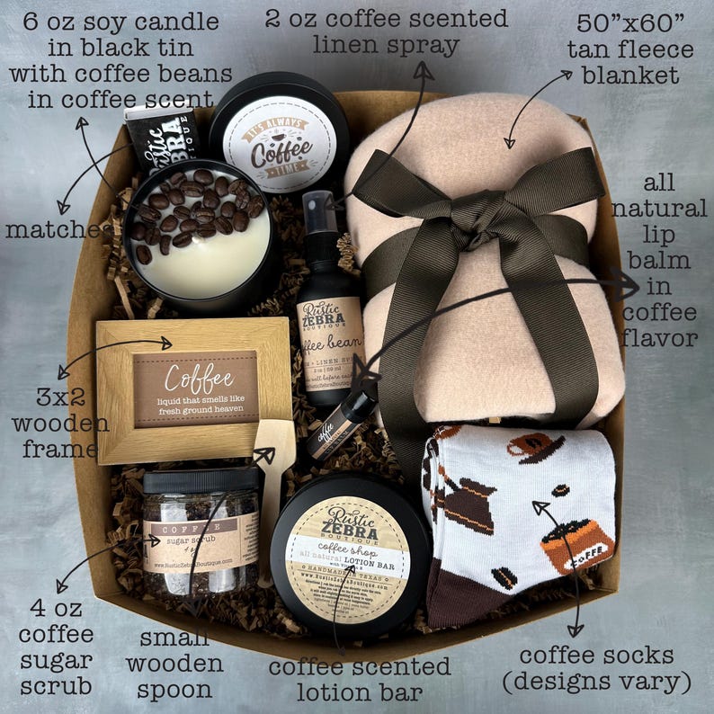 May include: A coffee-themed gift basket with a tan fleece blanket, coffee-scented lotion bar, coffee socks, a small wooden spoon, coffee sugar scrub, a 3x2 wooden frame with the word "Coffee" on it, a 6 oz soy candle in a black tin with coffee beans, a 2 oz coffee-scented linen spray, and a lip balm in coffee flavor.