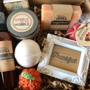 May include: A gift box filled with various items, including a jar with the text "Gobble 'Til You Wobble", a bar of orange oatmeal handmade soap, a lavender linen spray, and a small white framed picture with the text "I am so thankful for you."