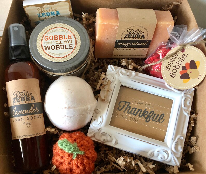 May include: A gift box filled with various items, including a jar with the text "Gobble 'Til You Wobble", a bar of orange oatmeal handmade soap, a lavender linen spray, and a small white framed picture with the text "I am so thankful for you."