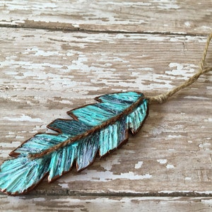 May include: A turquoise blue and copper feather ornament with a rustic twine hanger.
