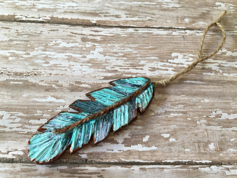 May include: A turquoise blue and copper feather ornament with a rustic twine hanger.