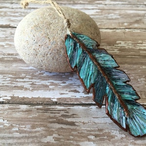 May include: A turquoise blue and copper feather pendant on a twine cord. The feather is textured and has a rustic look.