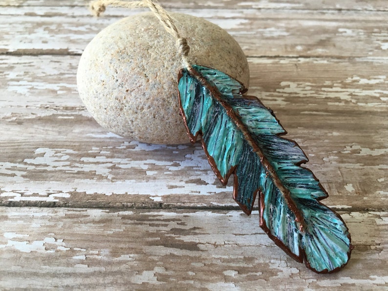 May include: A turquoise blue and copper feather pendant on a twine cord. The feather is textured and has a rustic look.