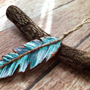 May include: A turquoise blue and copper colored feather ornament with a brown twine hanger. The feather is painted with a striped pattern and has a rustic look.