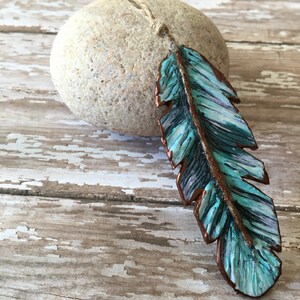 May include: A teal blue and copper colored feather ornament with a rustic twine hanger.