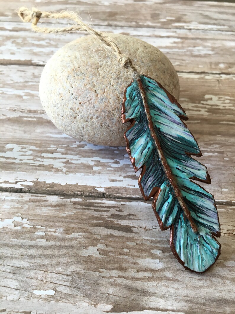 May include: A teal blue and copper colored feather ornament with a rustic twine hanger.