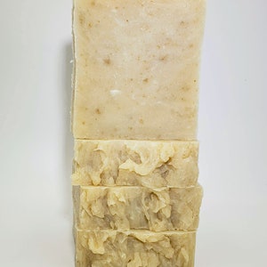 May include: A stack of four bars of handmade soap. The soap is a light beige color and has a textured surface.