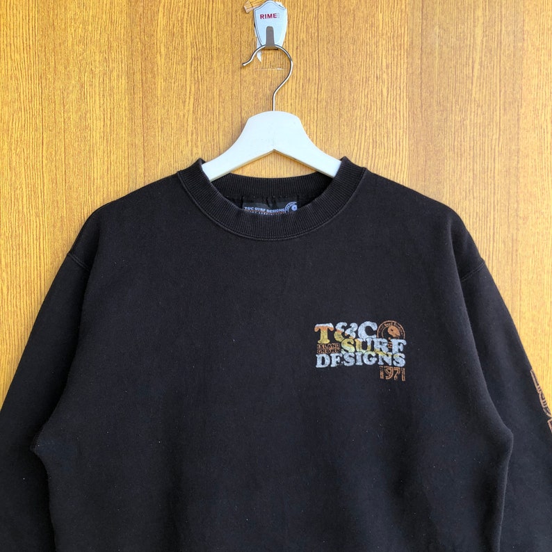 May include: Black sweatshirt with a colorful graphic print that reads "T&C Surf Designs 1971".