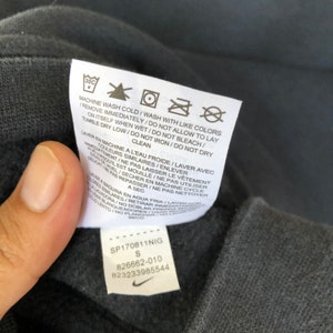 May include: A black care tag with white text and symbols. The tag includes washing instructions for a garment. The text reads "Machine wash cold/Wash with like colors/Remove immediately/Do not allow to lay on itself when wet/Do not bleach/Tumble dry low/Do not iron/Do not dry clean". The tag also includes a size "S" and the numbers "SP170811NIG", "826662-010", and "823233985544".
