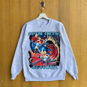 May include: Gray sweatshirt with a graphic print of Sonic the Hedgehog and a red character. The text "Spin into Action!" is printed on the sweatshirt.