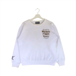 May include: White long-sleeved sweatshirt with a brown graphic print of "LEXUS Team Kraft Racing Development TRD Red Bull Racing International". The sweatshirt has a star on the left sleeve.