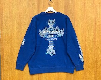 May include: Royal blue sweatshirt with a white and light blue graphic design on the back and sleeves. The design includes the word "PIKO" and the text "Hawaiian Longboard Wear". The sweatshirt is hanging on a white hanger.
