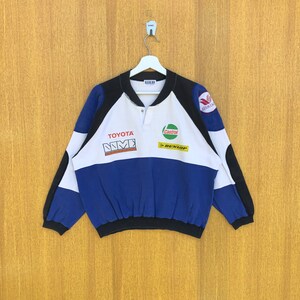 May include: A white, blue and black long-sleeved sweatshirt with a button-up collar. The sweatshirt features the logos of Toyota, Castrol and Dunlop on the front.