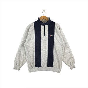 May include: A gray and navy blue quarter-zip sweatshirt with a vertical stripe design. The sweatshirt has a small logo on the right chest that says "SAIL" with a small flag graphic.