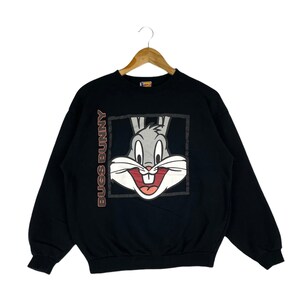 May include: Black sweatshirt featuring a large Bugs Bunny graphic on the front. The graphic is a close-up of Bugs Bunny's face with the text "Bugs Bunny" printed vertically on the left side of the graphic.