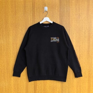 May include: Black sweatshirt with a gold and brown embroidered logo that says "T&C Surf Designs 1971". The sweatshirt has a crew neck and long sleeves.