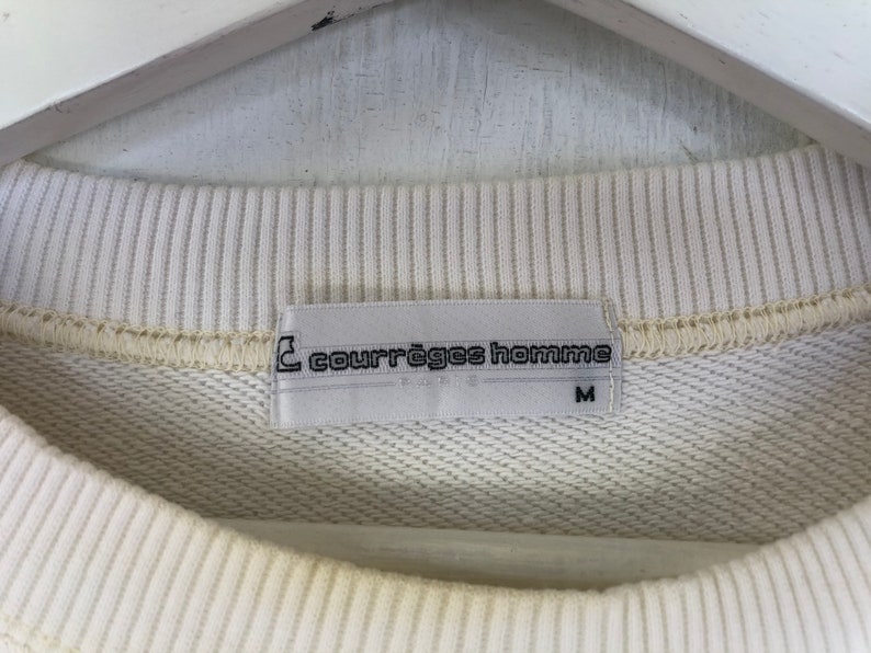 May include: A white sweatshirt with a white tag that reads "Courr&egrave;ges Homme" and "M" in black text.