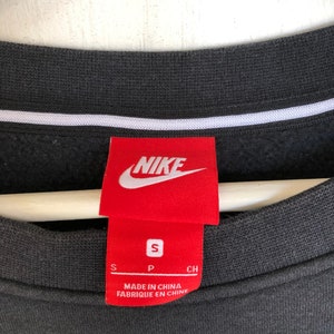 May include: Black Nike sweatshirt with a red Nike logo and size tag. The tag says "S" for size, "P" for "Made in China" and "CH" for "Fabrique en Chine".