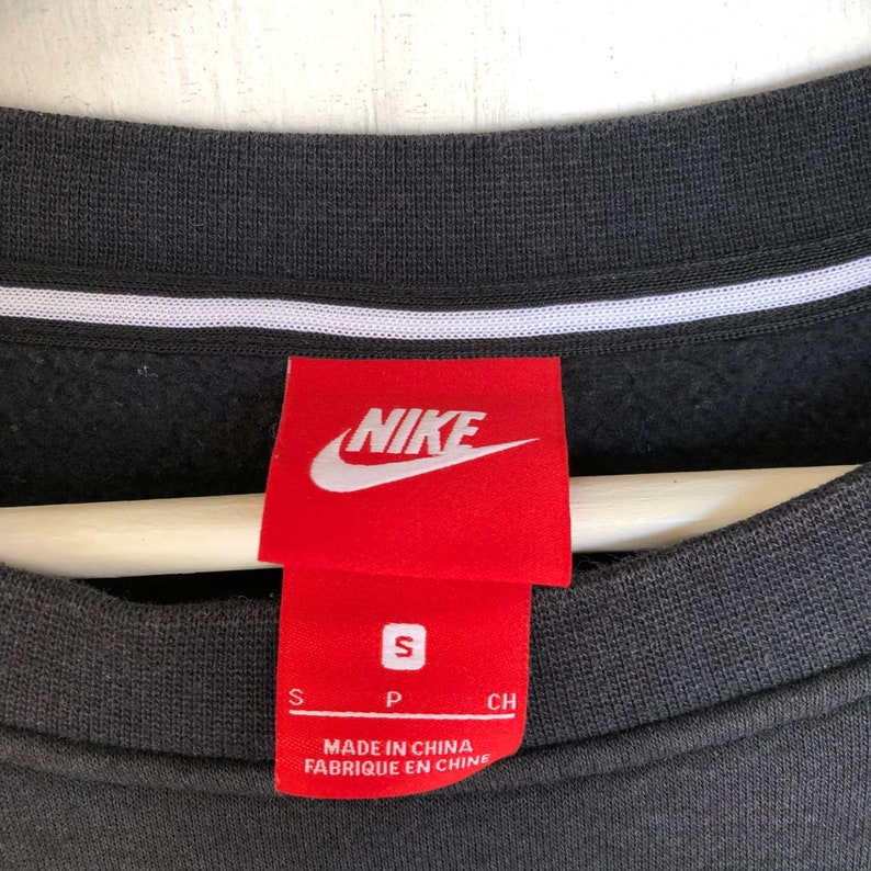 May include: Black Nike sweatshirt with a red Nike logo and size tag. The tag says "S" for size, "P" for "Made in China" and "CH" for "Fabrique en Chine".