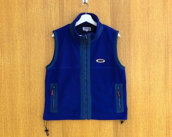 May include: A blue fleece vest with a zipper closure, two pockets, and a small logo on the front. The vest has a drawstring at the bottom.