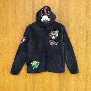 May include: A dark blue fleece zip-up hoodie with a hood and multiple patches. The patches feature a shamrock, a palm tree, and the text "Hawaii Aloha Style" and "Local Motion".