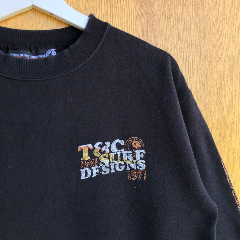 May include: Black sweatshirt with a brown and orange graphic print that says "T&C Surf Designs 1971" and a small logo of a surfer with a wave.