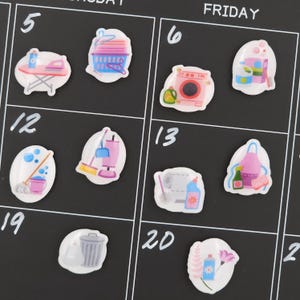 May include: A black calendar with white numbers and the word "FRIDAY" at the top. The calendar features various cleaning-themed stickers, including a washing machine, mop, and cleaning supplies.