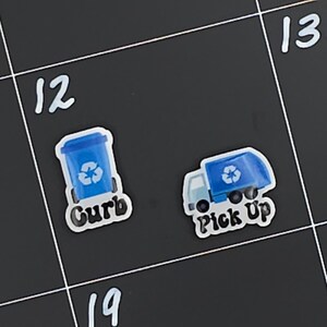 May include: Two blue recycling stickers on a black background. The left sticker shows a blue recycling bin with a recycle symbol and the word "Curb". The right sticker shows a blue recycling truck with a recycle symbol and the words "Pick Up".