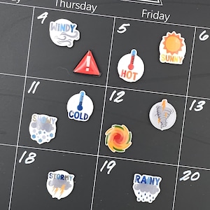 May include: A black calendar grid with weather-themed stickers. Stickers include "WINDY", a red triangle, "HOT", "SUNNY", "COLD", "SNOWY", a colorful swirl, "STORMY", and "RAINY".