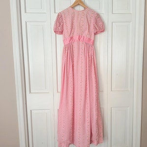 Puede incluir: Un vestido maxi rosa con estampado floral y mangas cortas. El vestido tiene un corpiño ajustado y una falda fluida.