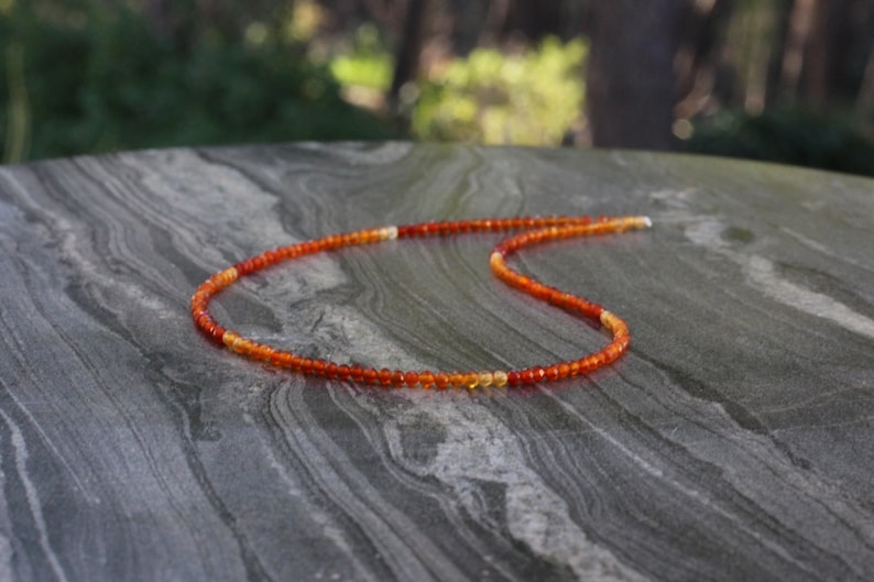 Puede incluir: Un collar delicado hecho de peque&ntilde;as cuentas redondas de cornalina en tonos naranja y rojo. Las cuentas est&aacute;n enhebradas en una fina cadena de plata.
