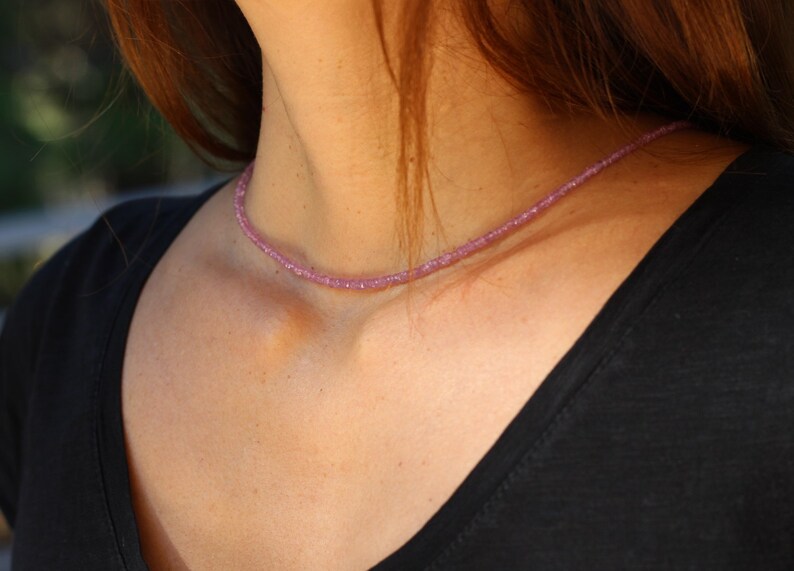 May include: A delicate pink gemstone necklace with small, evenly spaced beads. The necklace is worn by a person with long brown hair.