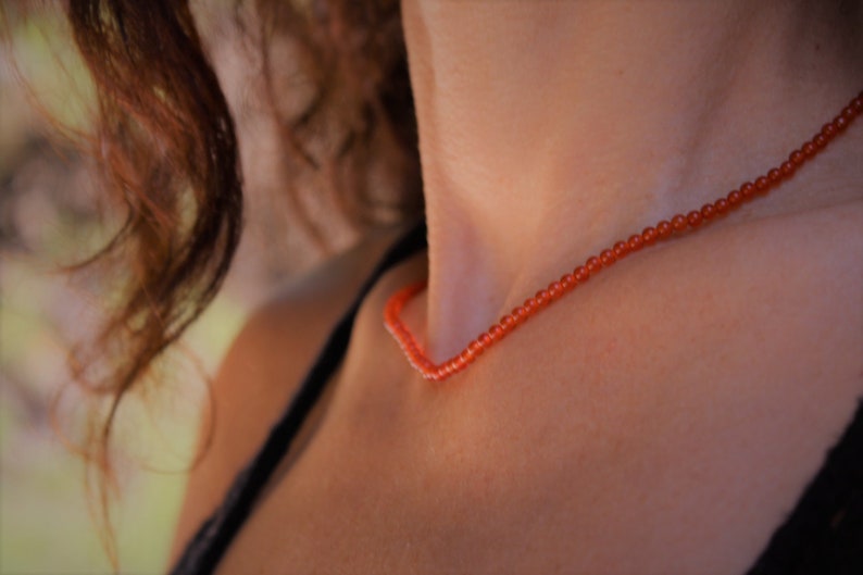 Puede incluir: Primer plano de una persona que lleva un collar hecho de peque&ntilde;as cuentas naranjas.