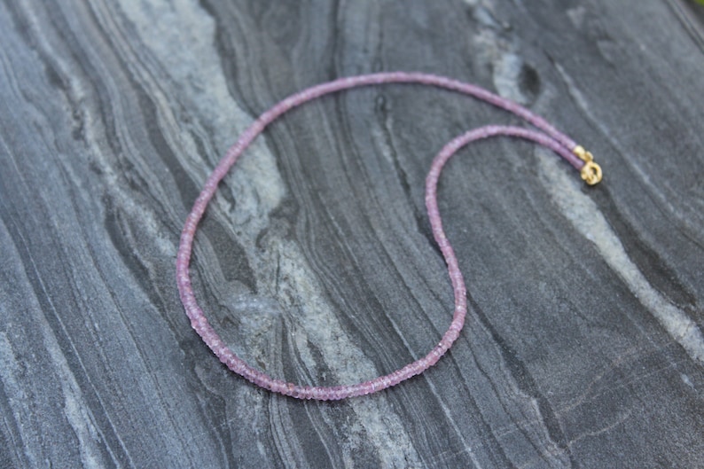 May include: A delicate pink gemstone necklace with a gold clasp. The necklace is made of small, round beads and is approximately 18 inches long.
