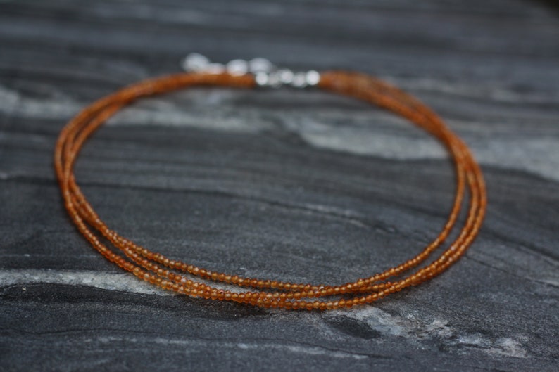 Puede incluir: Un delicado collar de varios hilos hecho de peque&ntilde;as cuentas de color marr&oacute;n anaranjado. El collar est&aacute; sobre una superficie gris oscura.