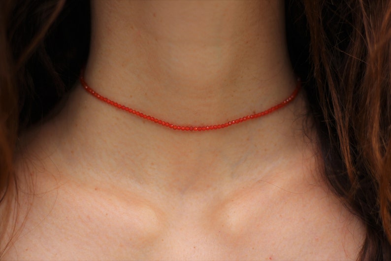 Puede incluir: Un delicado collar de cuentas rojas que se lleva en el cuello.