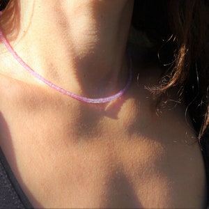 May include: A delicate purple gemstone necklace with small, evenly spaced beads. The necklace is worn by a person with long brown hair.