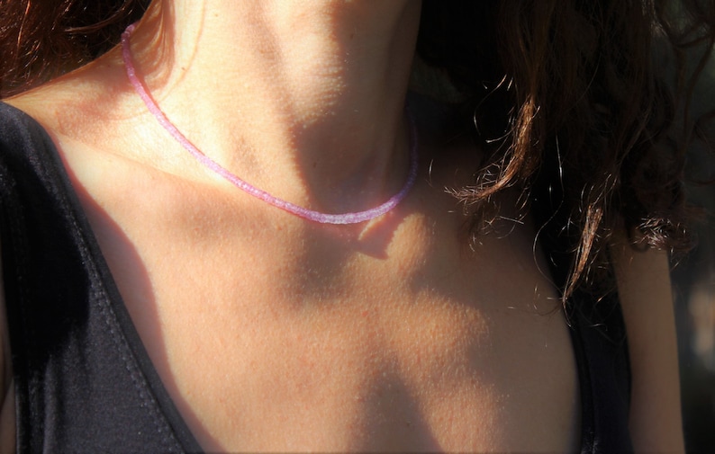 May include: A delicate purple gemstone necklace with small, evenly spaced beads. The necklace is worn by a person with long brown hair.