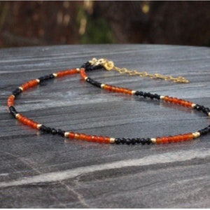Puede incluir: Un collar delicado con cuentas negras y naranjas alternas. El collar est&aacute; hecho con cuentas peque&ntilde;as y redondas y tiene un cierre de cadena dorada.